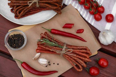 Photo of Delicious kabanosy with rosemary, peppercorn, garlic and chilli pepper on wooden table, flat lay
