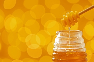 Photo of Honey pouring from dipper into jar on blurred background. Space for text