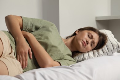 Young woman suffering from menstrual pain on bed at home