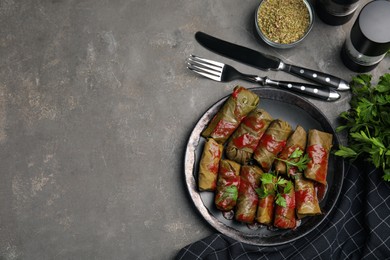 Delicious stuffed grape leaves with tomato sauce on grey table, flat lay. Space for text