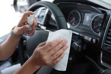 Woman cleaning steering wheel with wet wipe and antibacterial spray in car, closeup