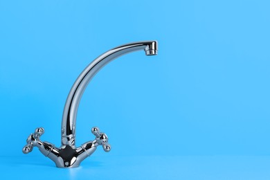Double handle water tap on light blue background. Space for text