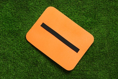 Orange foam seat mat for tourist on green grass, top view