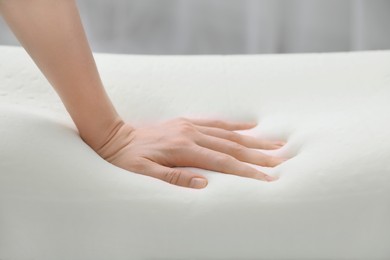 Photo of Woman touching orthopedic memory foam pillow indoors, closeup
