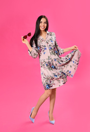 Young woman wearing floral print dress with stylish sunglasses on pink background