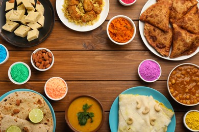 Frame of traditional Indian food and color powders on wooden table, flat lay with space for text. Holi festival celebration