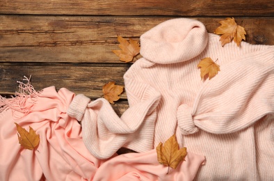 Pink sweater, scarf and dry leaves on wooden background, flat lay. Autumn season