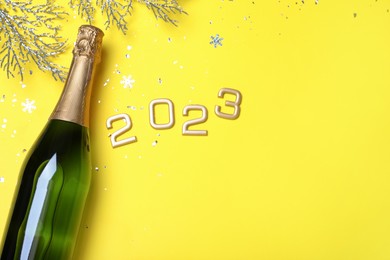 Happy New Year 2023! Flat lay composition with bottle of sparkling wine on yellow background, space for text