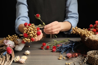 Florist making bouquet of dried flowers at wooden table, closeup