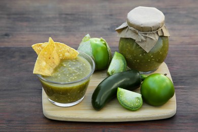 Photo of Delicious salsa sauce with tortilla chips and ingredients on wooden table
