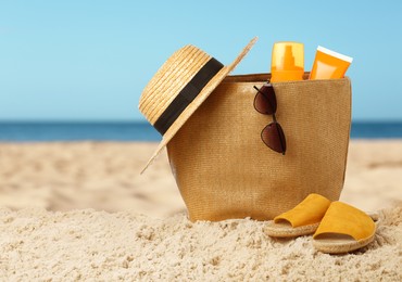 Stylish bag with different accessories on sandy beach near ocean