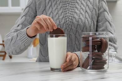 Woman dipping delicious choco pie into glass of milk at white marble table, closeup