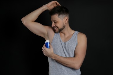 Handsome man applying deodorant on black background