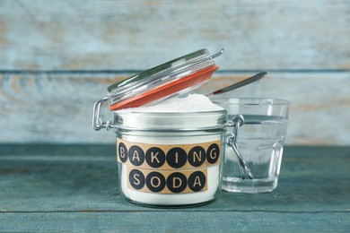 Jar with baking soda and glass of water on light blue wooden table