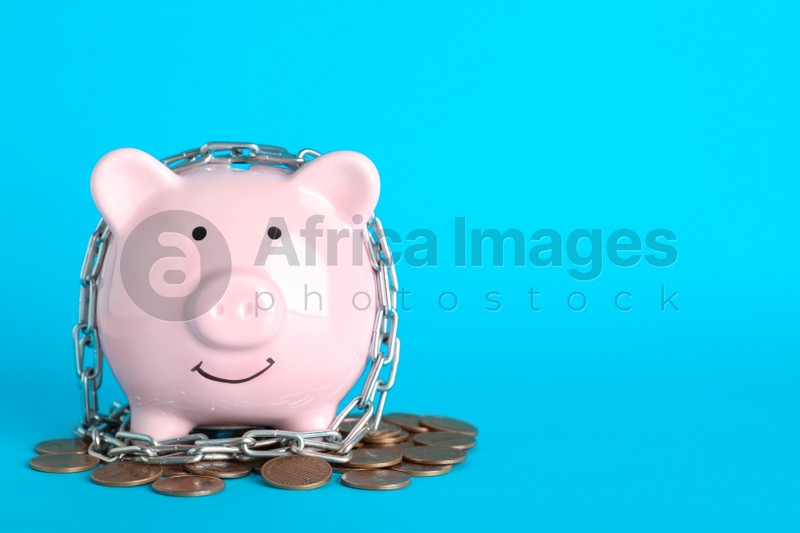 Piggy bank  with steel chain and coins on light blue background, space for text. Money safety concept