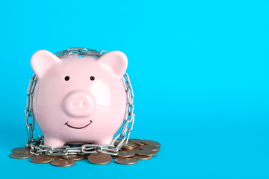 Piggy bank  with steel chain and coins on light blue background, space for text. Money safety concept