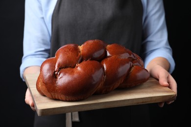 Closeup view of woman holding homemade braided bread on black background. Traditional Shabbat challah