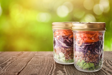 Jars with healthy meal on wooden table against blurred background, space for text