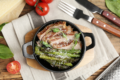 Tasty meat served with asparagus and sprouts in portioned frying pan on table, flat lay