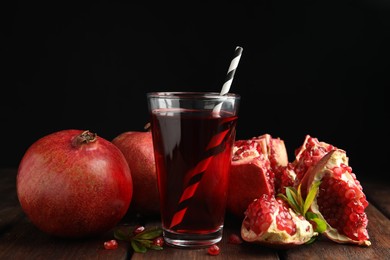 Photo of Pomegranate juice and fresh fruits on wooden table against black background