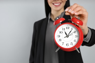 Businesswoman holding alarm clock on light grey background, closeup with space for text. Time management
