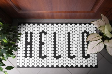 Stylish door mat with word HELLO and houseplants on floor, top view