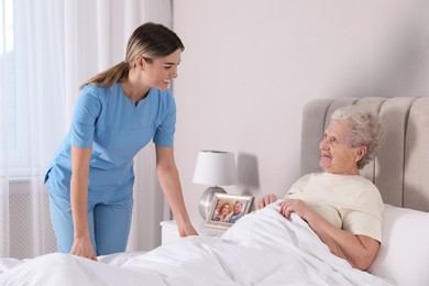 Young caregiver assisting senior woman in bedroom. Home health care service