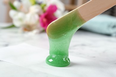 Applying wax on paper with spatula at white marble table, closeup