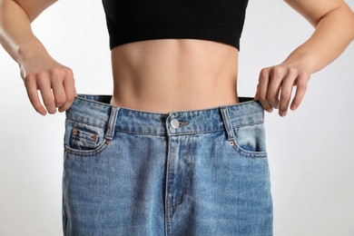 Skinny woman in oversized jeans on light background, closeup. Weight loss concept