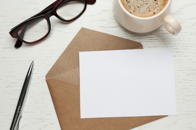 Envelope with blank paper card, cup of coffee, pen and glasses on white wooden table, flat lay