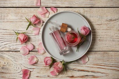 Flat lay composition with essential rose oil and flowers on white wooden table
