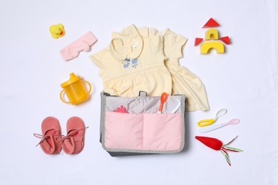 Composition with maternity bag and baby accessories on white background, top view