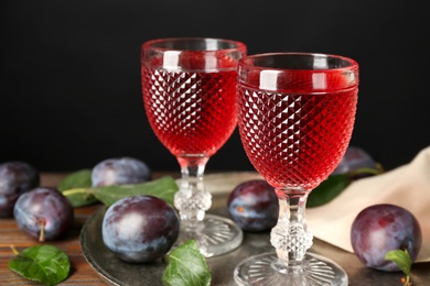 Delicious plum liquor and ripe fruits on wooden table against black background. Homemade strong alcoholic beverage
