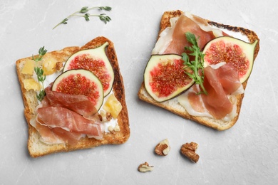 Delicious sandwiches with figs, proscuitto and cheese on light table, flat lay