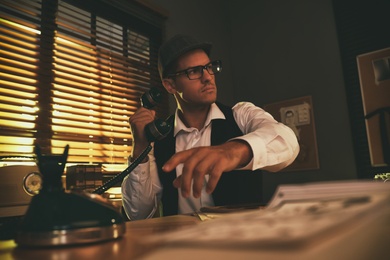 Old fashioned detective dialing telephone number at table in office