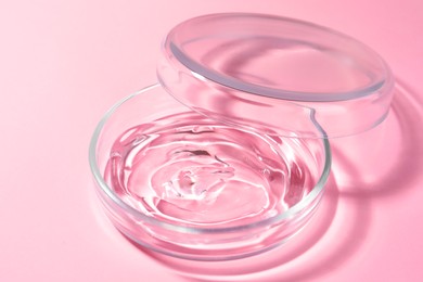Petri dish with liquid and lid on pale pink background, closeup