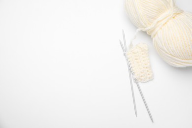 Soft woolen yarn, knitting and metal needles on white background, top view