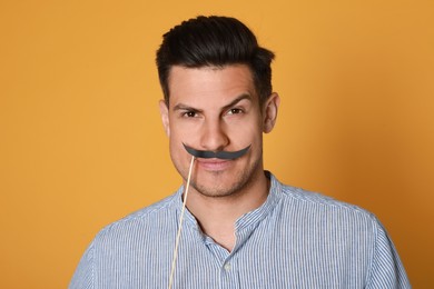 Photo of Funny man with fake mustache on yellow background