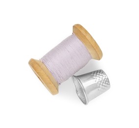 Photo of Thimble and spool of violet sewing thread isolated on white, top view