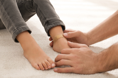 Father putting sticking plaster onto little son's leg indoors, closeup