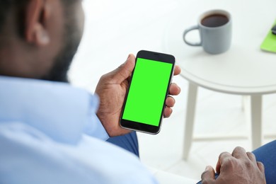 Image of Chroma key compositing. African American man holding smartphone with green screen indoors, closeup. Mockup for design