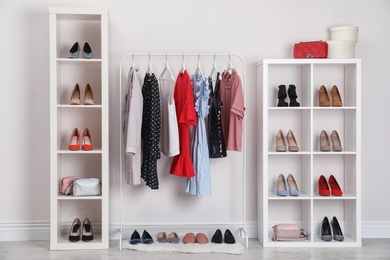 Photo of Wardrobe shelves with different stylish shoes and clothes indoors. Idea for interior design