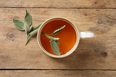 Photo of Cup of aromatic sage tea and fresh leaves on wooden table, flat lay