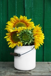 Photo of Bouquet of beautiful sunflowers in tin on wooden table near green wall