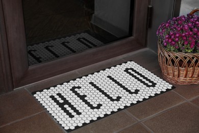 Stylish door mat with word HELLO and beautiful flowers near entrance
