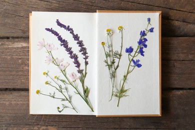 Open book with beautiful dried flowers on wooden table, top view