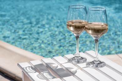 Photo of Glasses of tasty wine on wooden table near swimming pool, space for text