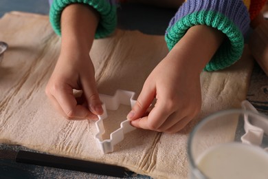 Little child cutting Christmas cookies at blue wooden table, closeup