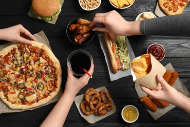Photo of Friends eating pizza, chicken wings and other fast food at black wooden table, top view