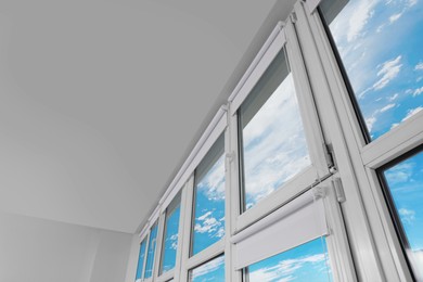 Photo of Plastic windows with white roller blinds indoors, low angle view